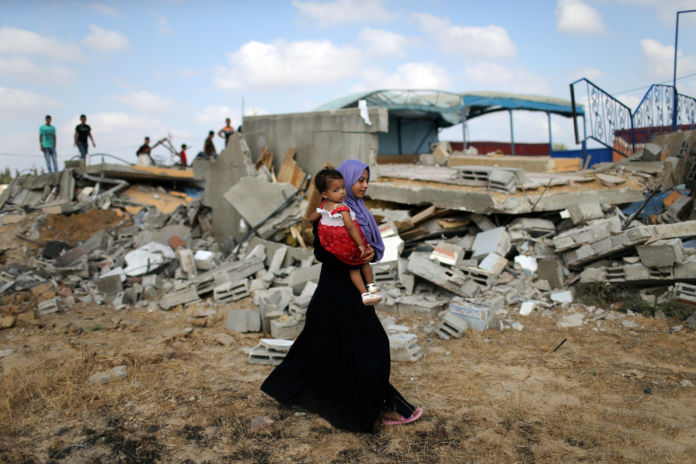 Palestinian woman carries a girl as she walks past the site of an Israeli air strike, in Khan Younis in the southern Gaza Strip